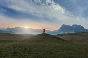hiker standing in silhouette at dawn on the meadows of the alpe di siusi, in the background the Sassolungo / Langkofel, Dolomites, Kastelruth, South Tyrol, Italy hiker standing in silhouette at dawn on the meadows of the alpe di siusi, in the background the Sassolungo / Langkofel, Dolomites, Kastelruth, South Tyrol, Italy